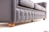 Dettaglio laterale di un divano Chesterfield in pelle nera, con piedino in legno intagliato in evidenza.