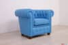 Poltrona Chesterina stile Chesterfield in pelle azzurro cielo saturo, vista angolata per evidenziare braccioli e lavorazione capitonné.