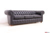 Vista angolare di un divano Chesterfield in pelle nera, con braccioli arrotolati e lavorazione capitonné in risalto.