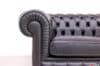 Primo piano del bracciolo arrotolato di un divano Chesterfield in pelle nera, con la tipica forma ricurva in risalto.